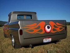Custom gray pickup truck with orange flame decals parked in a grassy field under a blue sky