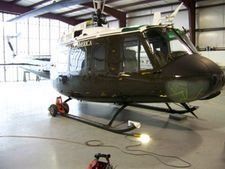 Dark green helicopter parked inside a hangar, with cables on the floor.