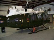 Dark green U.S. Marine helicopter parked inside a hangar with maintenance gear nearby