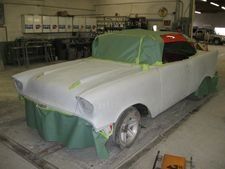 Car covered in white masking paper and green plastic in an auto body shop