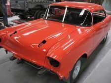 Red classic car body in a workshop, with hood and front lights removed, being restored