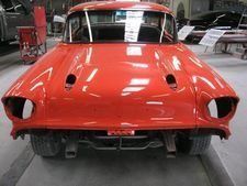 Front view of a red classic car body in a workshop, missing headlights and grille