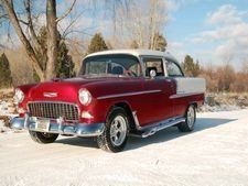 Classic red and white vintage car parked on a snowy road with trees in the background