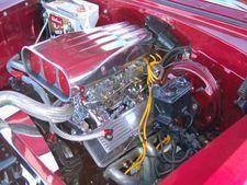 Red car engine bay with chrome intake and yellow wiring in a custom hot rod.