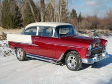 Red and white classic car parked on a snowy road with trees in the background