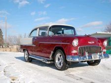 Classic red-and-white vintage car parked on snowy ground under a blue sky