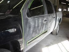 Gray pickup truck with black front end in a body shop, masked for painting