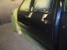 Black pickup truck in a garage, partially covered with green masking paper for painting