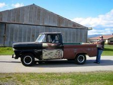 Rusty black-and-red vintage pickup truck parked by a barn, with a person standing at the bed