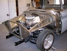 Partially assembled silver car chassis with exposed engine in a garage