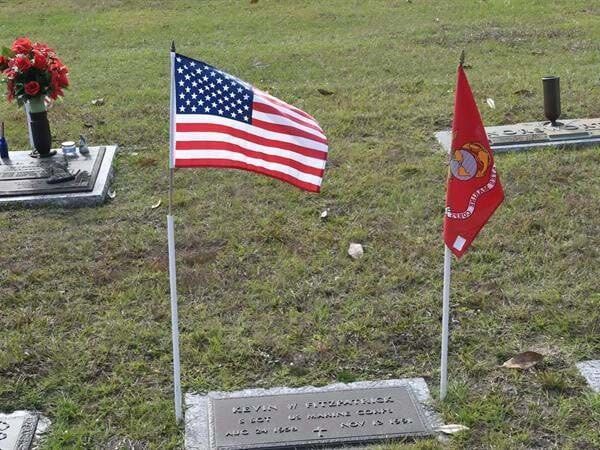 An american flag and a marine flag are on a grave in a cemetery
