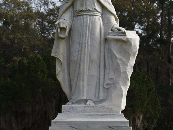 A statue of jesus is standing in a cemetery with trees in the background