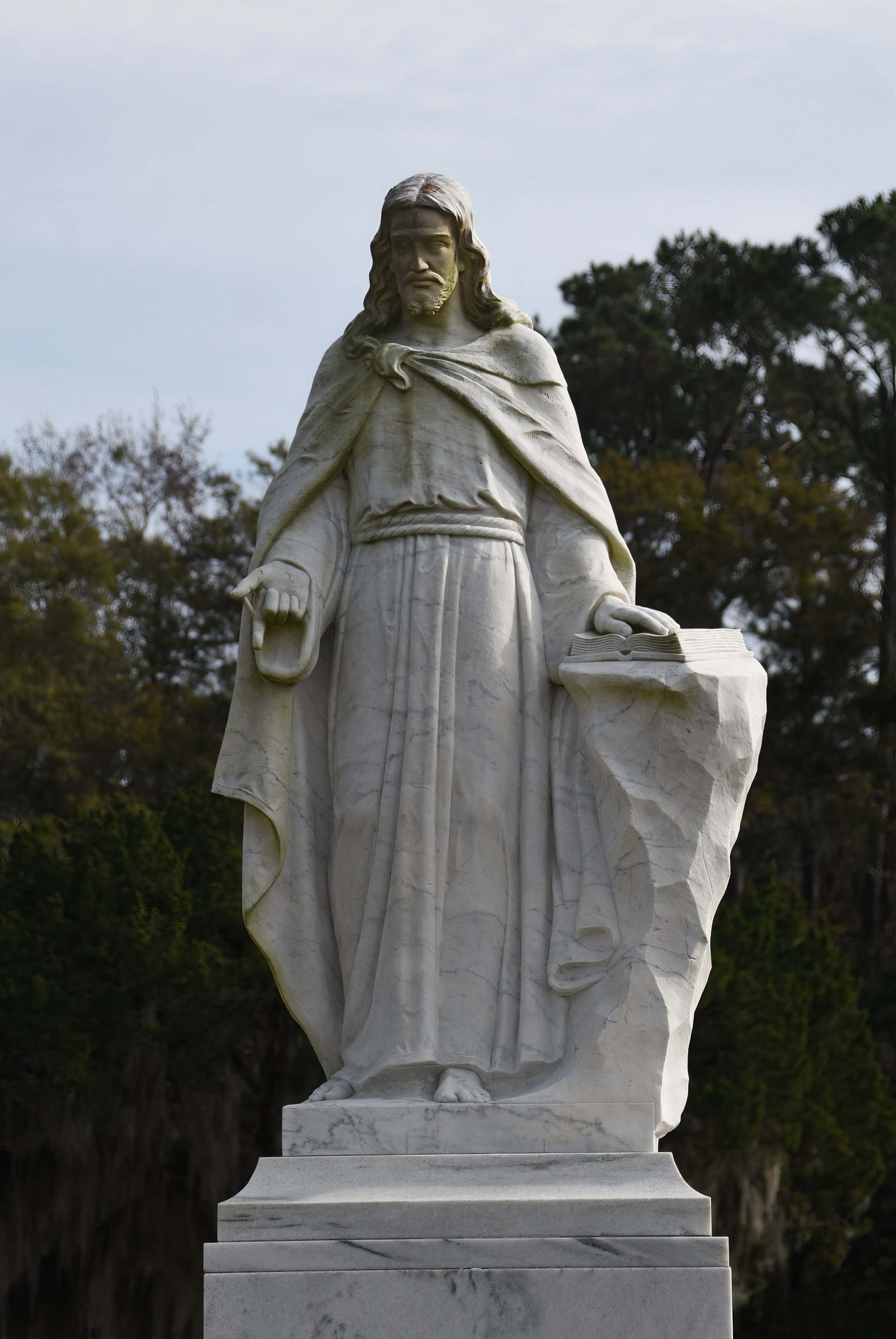 A statue of jesus is standing in a cemetery