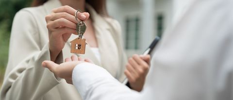 Handing over a house key to a person holding a phone, with a keychain visible