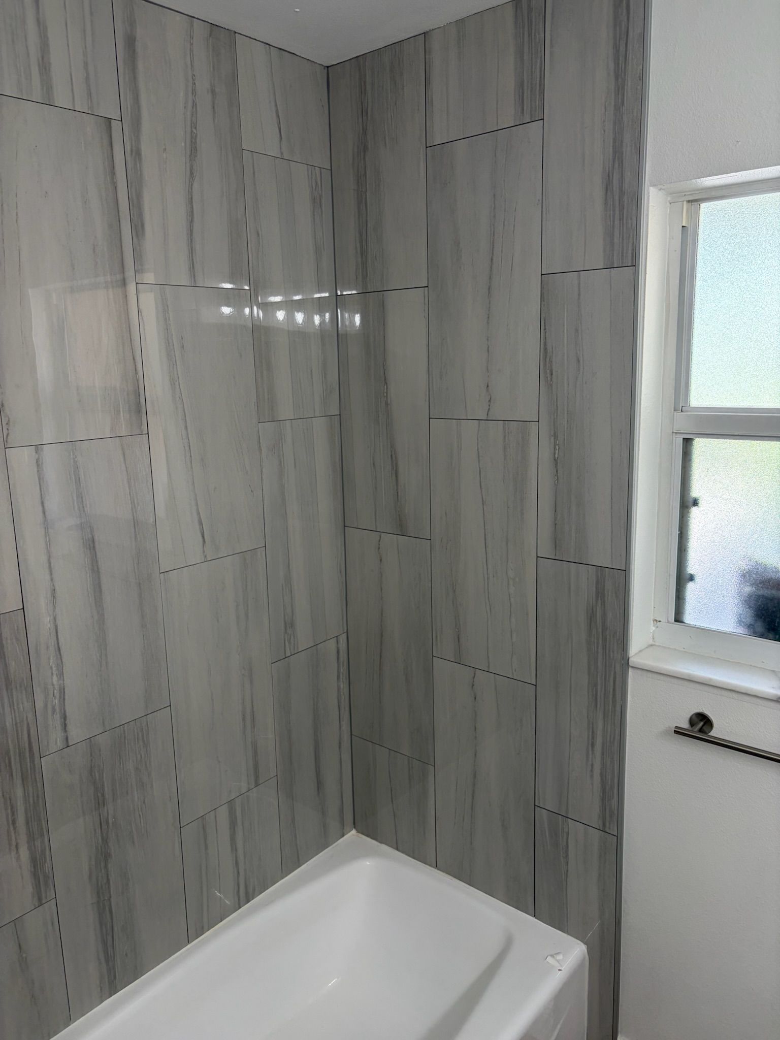 Tiled bathroom corner with a white bathtub and a window with frosted glass above a radiator.