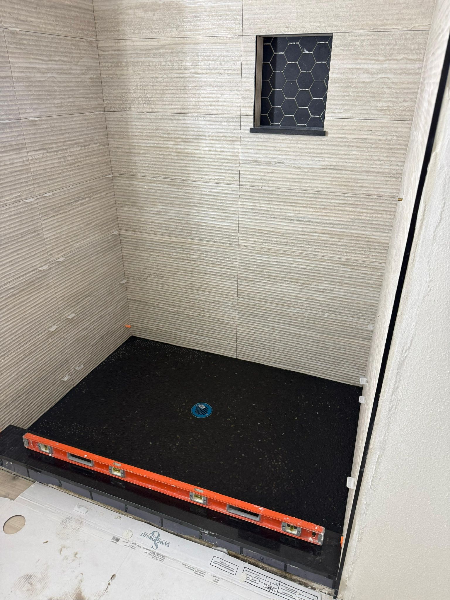 Empty indoor shower stall with tiled walls and a black shower base with a drain cover.