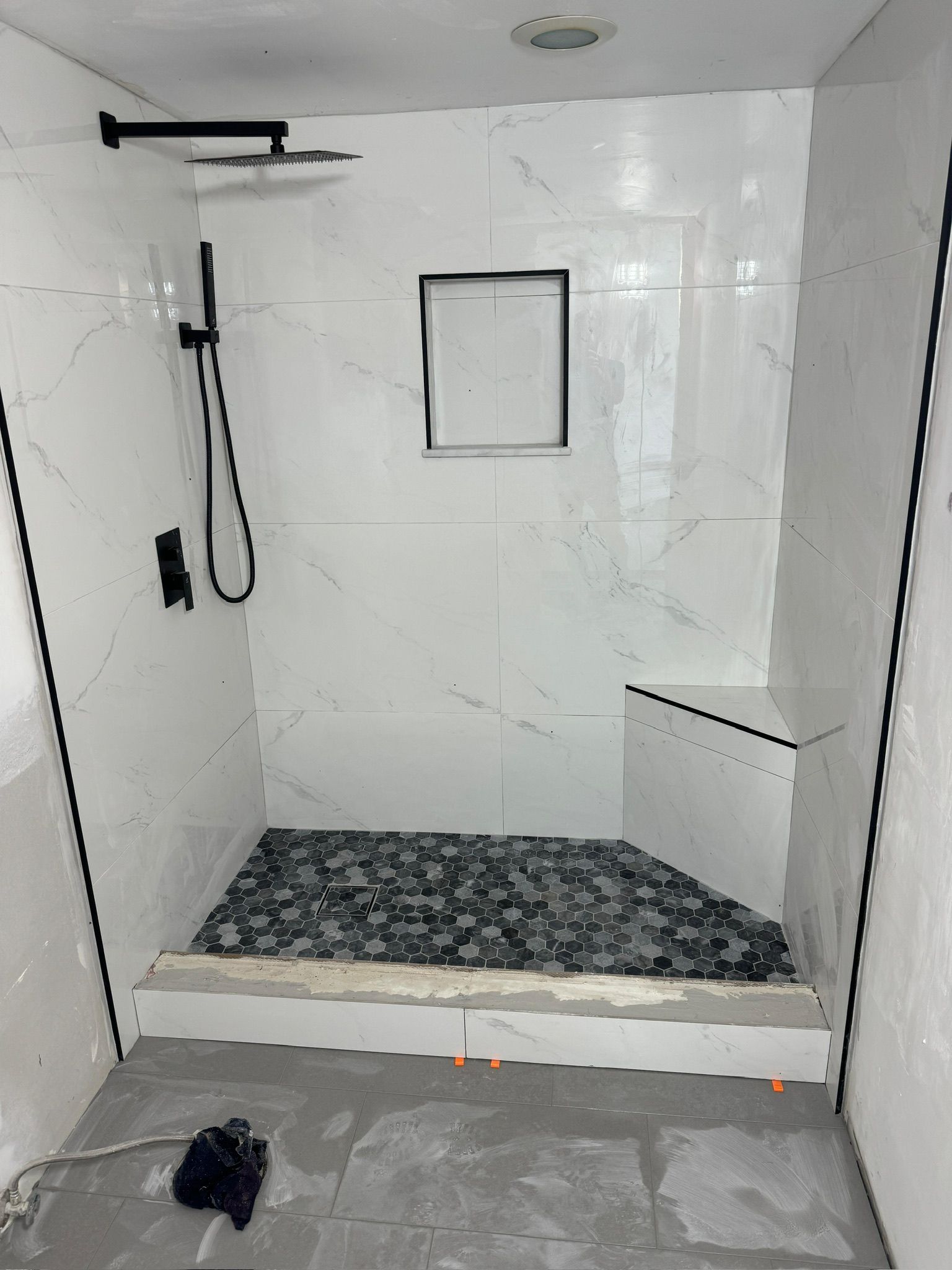 Tiled walk-in shower with black rainfall showerhead, built-in shelf, and pebble floor in a white bathroom