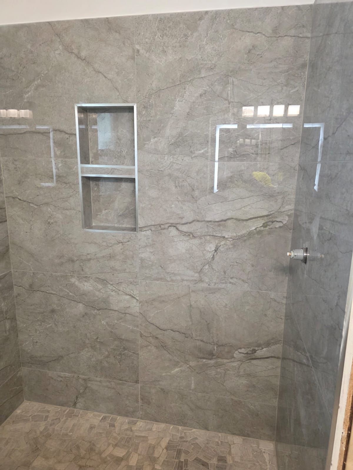 Modern tiled shower with a small window and glass door corner shelf