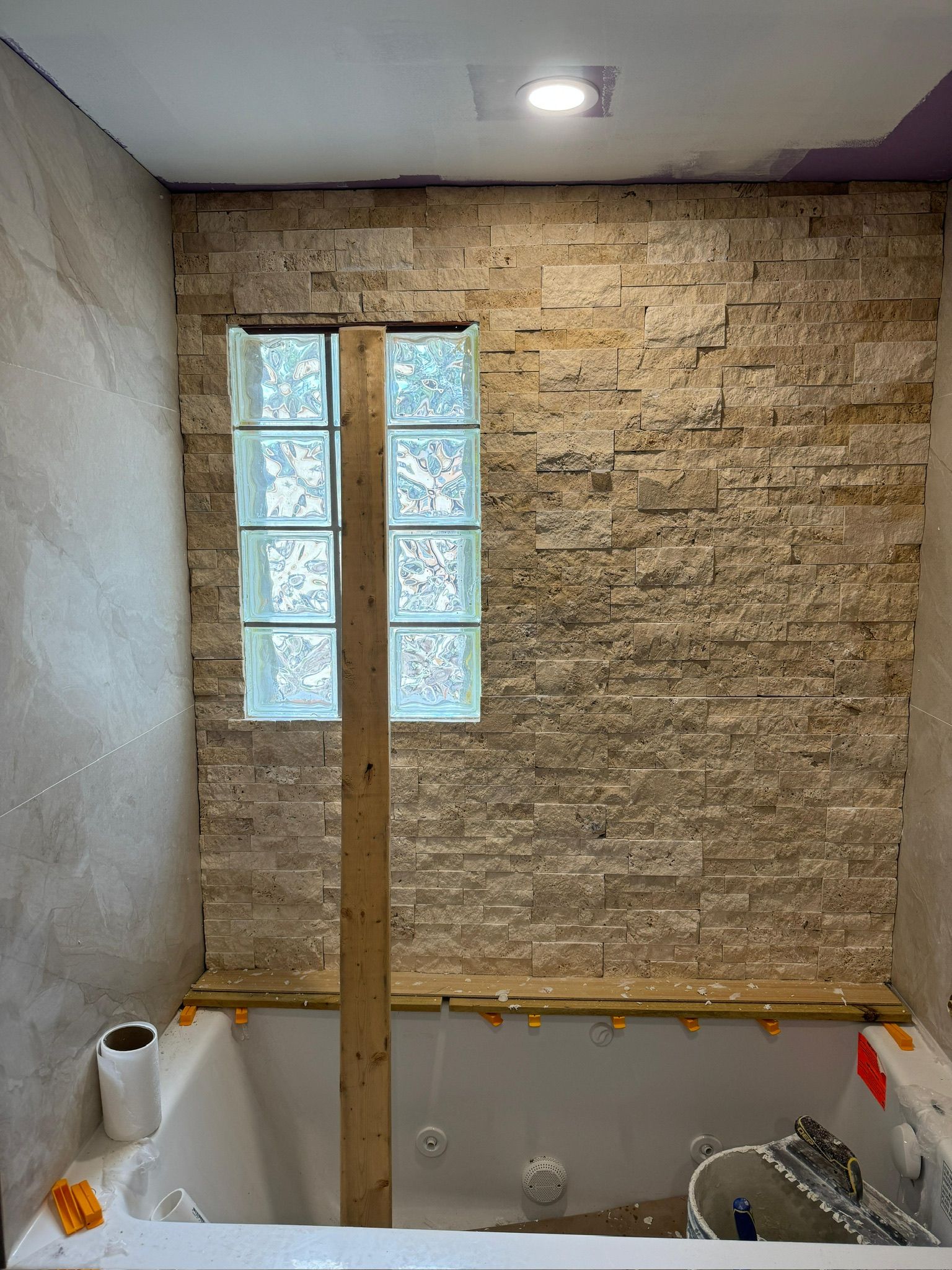 Small bathroom under renovation with exposed brick wall, narrow frosted windows, and construction materials.