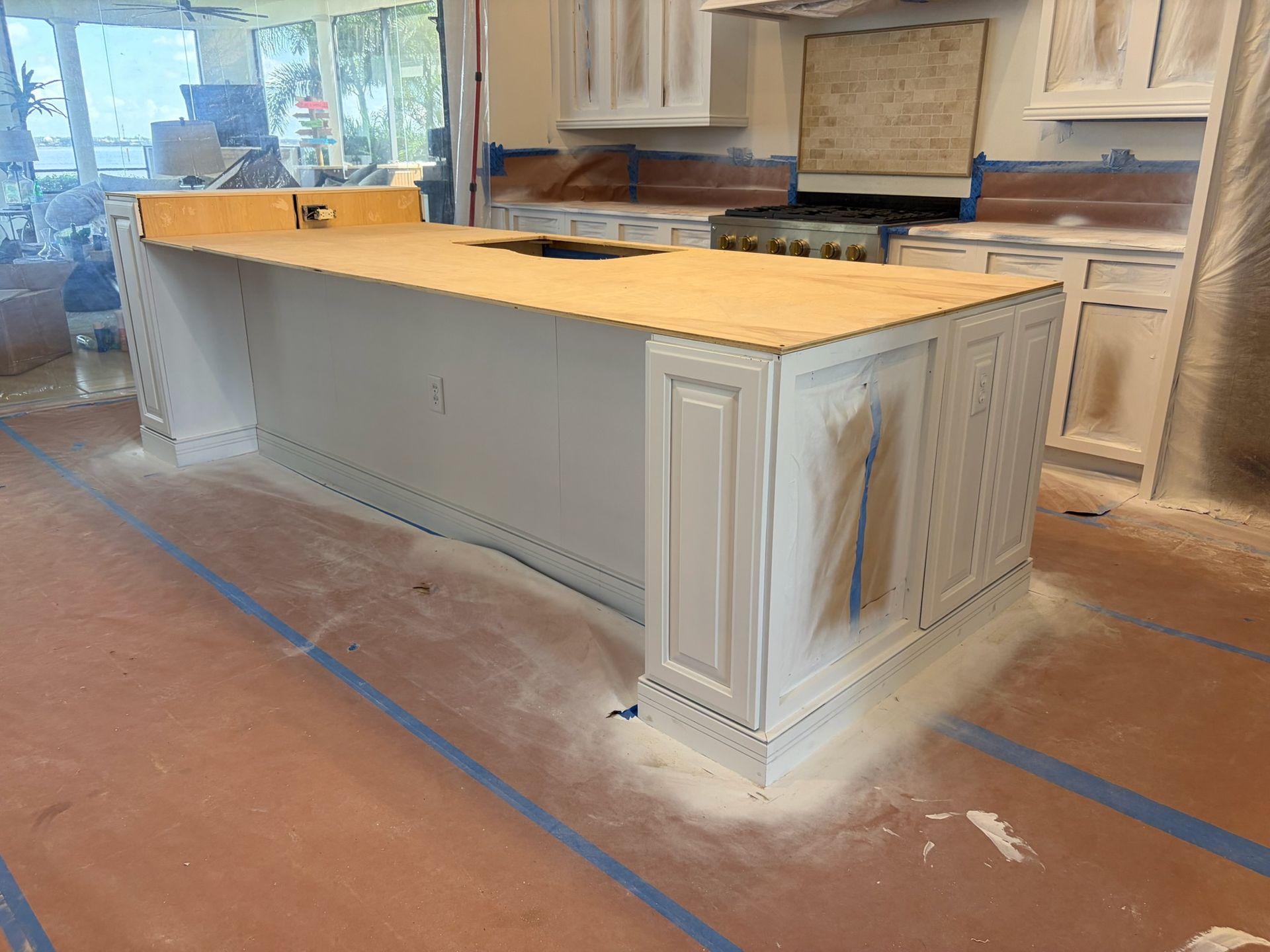 Kitchen island under construction with light wood cabinets, gray panels, and a tan countertop in a workshop.