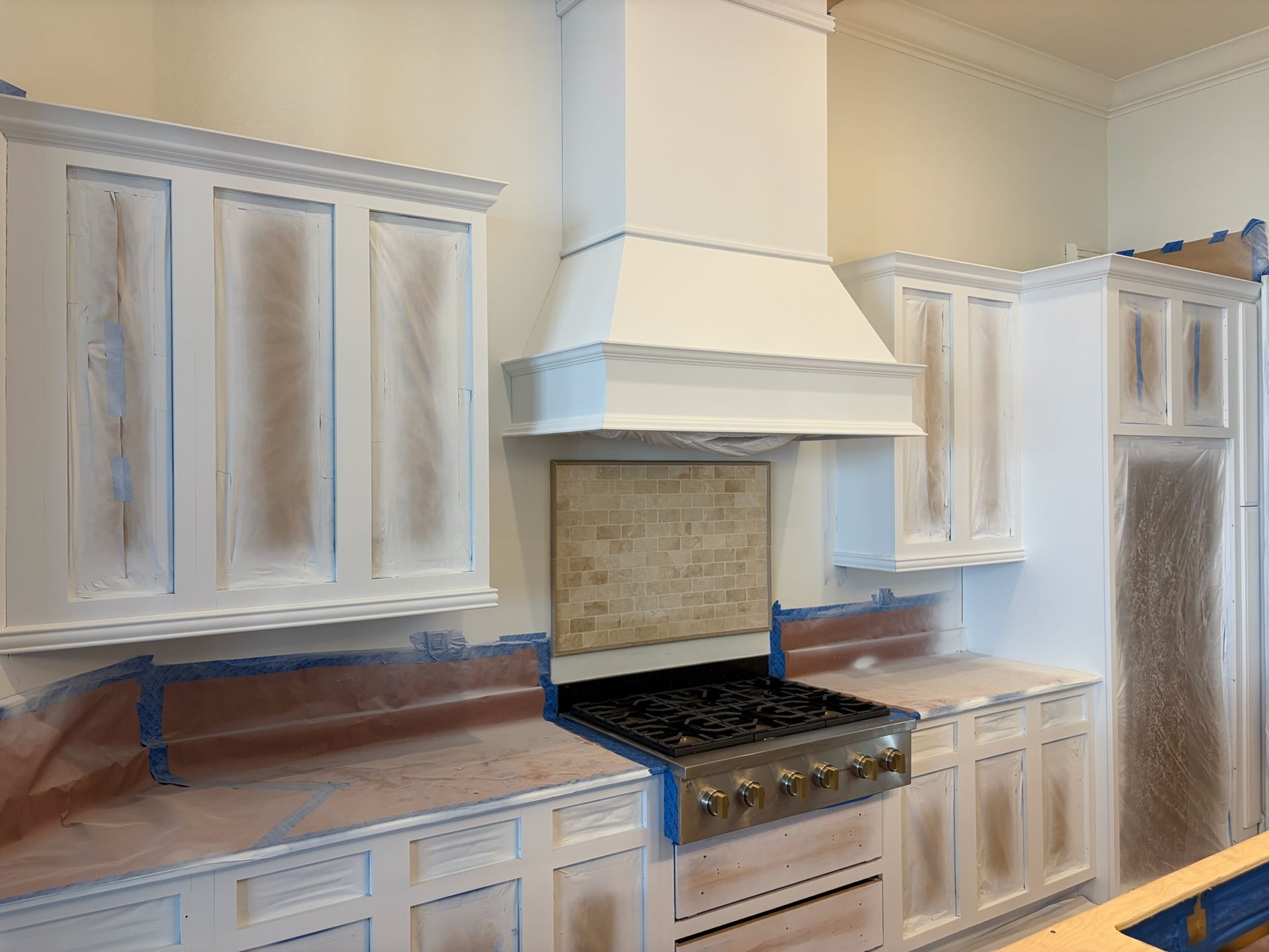 Bright kitchen with white cabinets, beige backsplash, black stove, and large white range hood