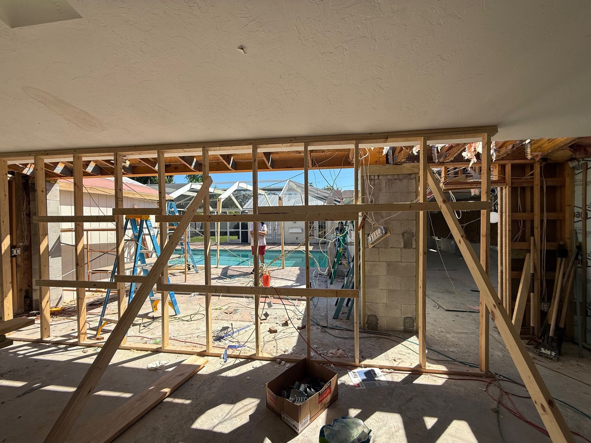 Interior wall framing during construction, revealing a pool area through a window.