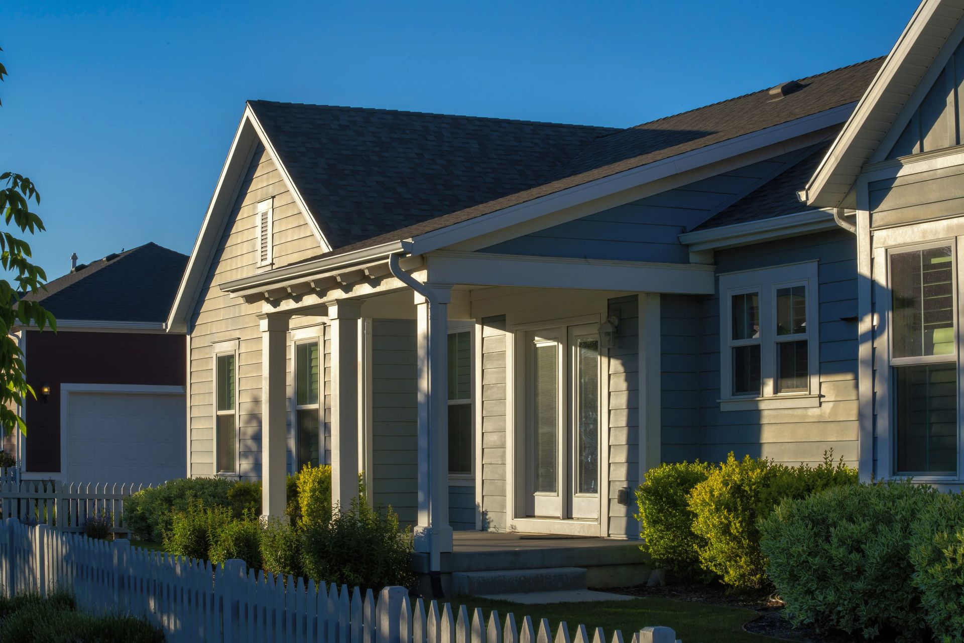 Sunlit suburban house with gray siding, white trim, front porch, and picket fence