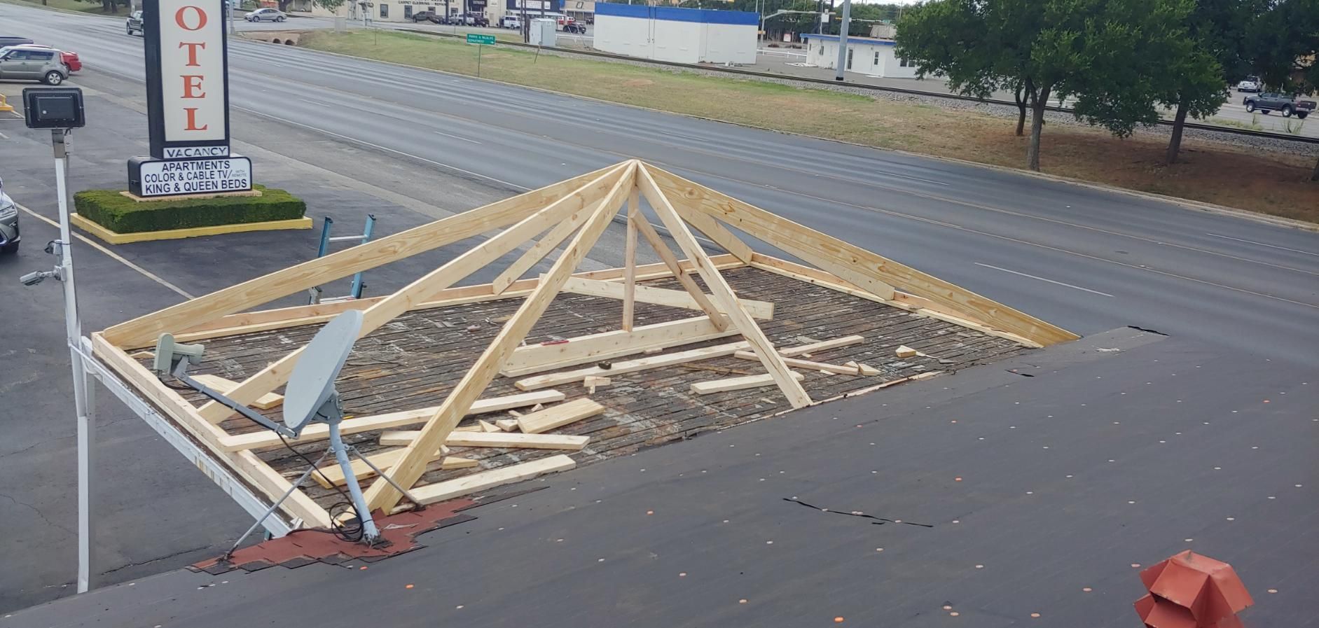 Collapsed wooden roof frame on a road beside a motel sign, with debris scattered across the pavement.