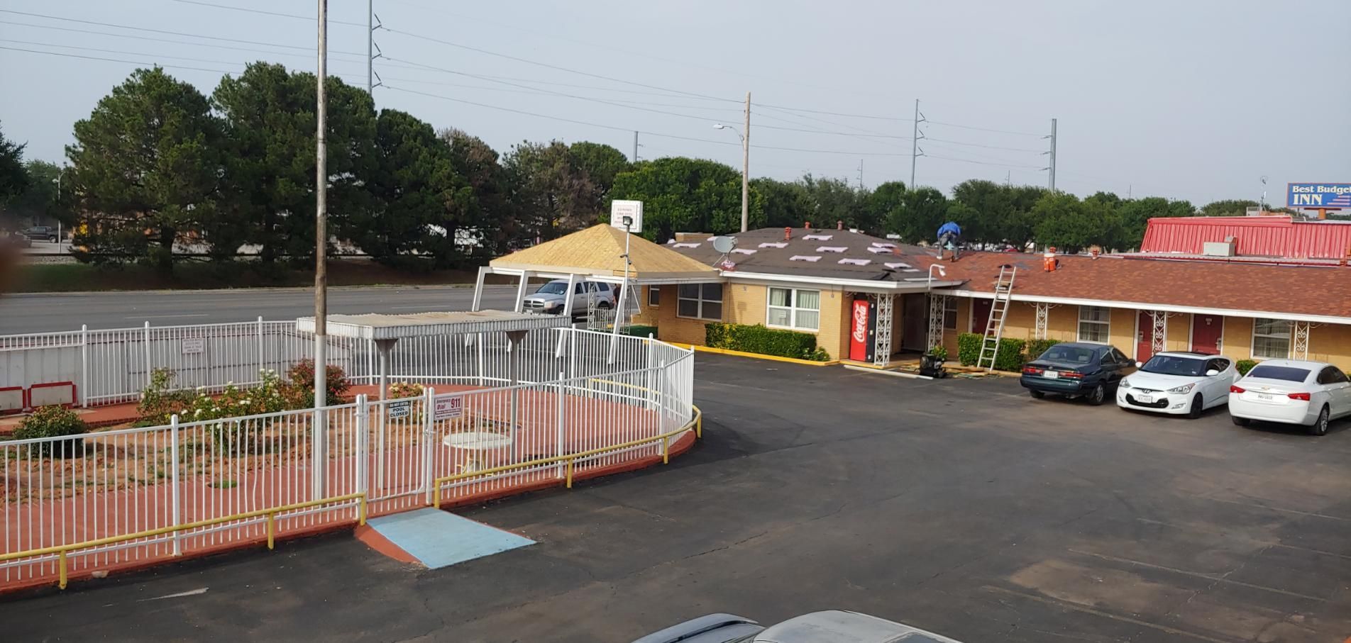 Parking lot outside a small motel with white cars, a yellow office, and trees in the background