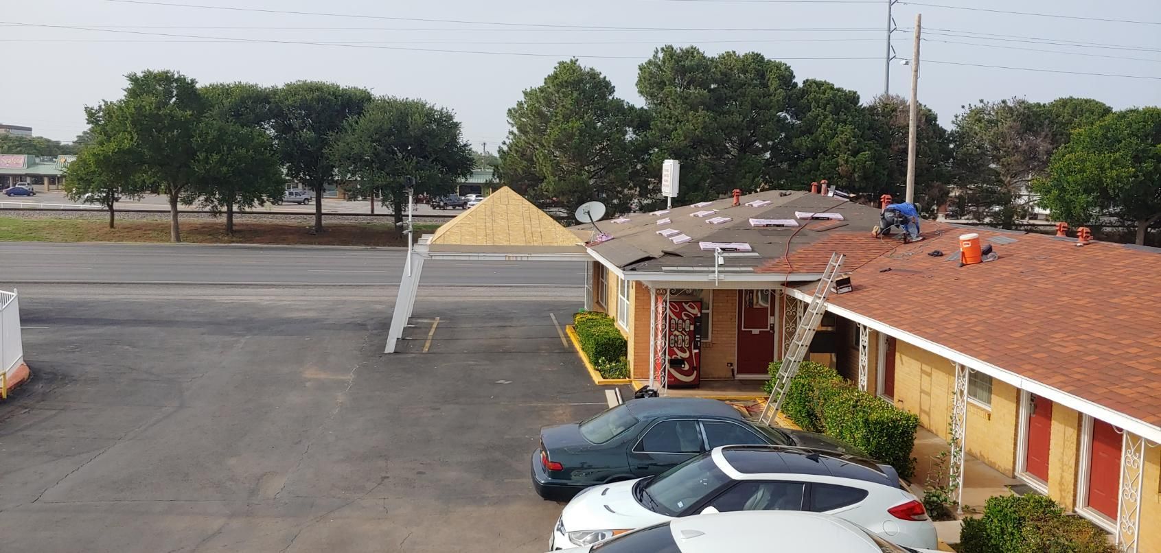 Motel parking lot with red-roofed rooms, several parked cars, and trees in the background
