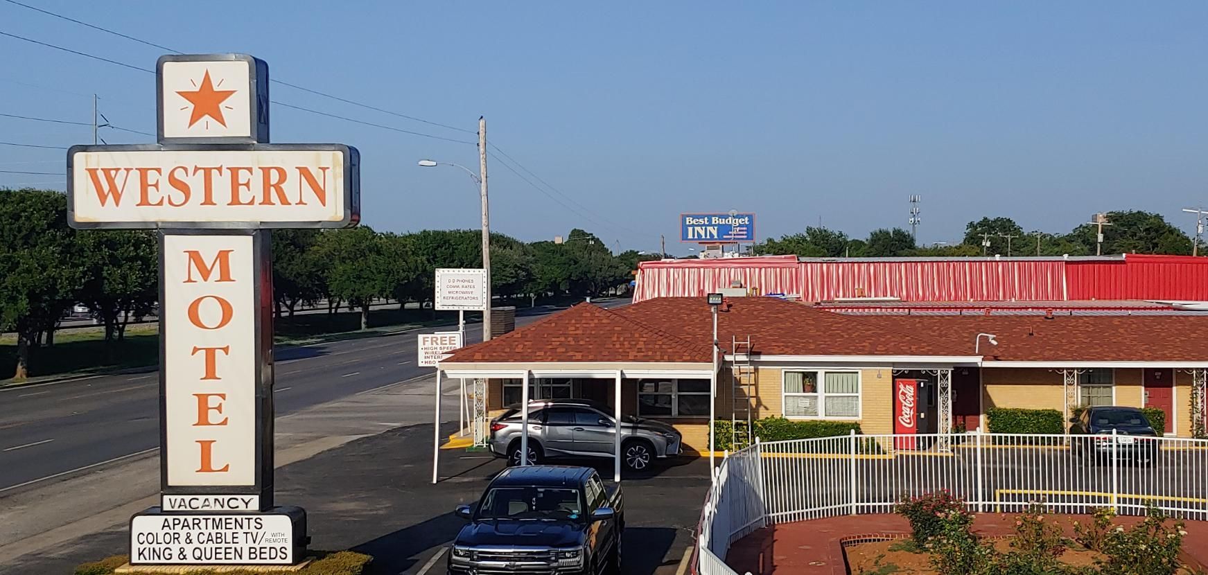Western Motel sign beside a red-roofed motel parking lot under a blue sky