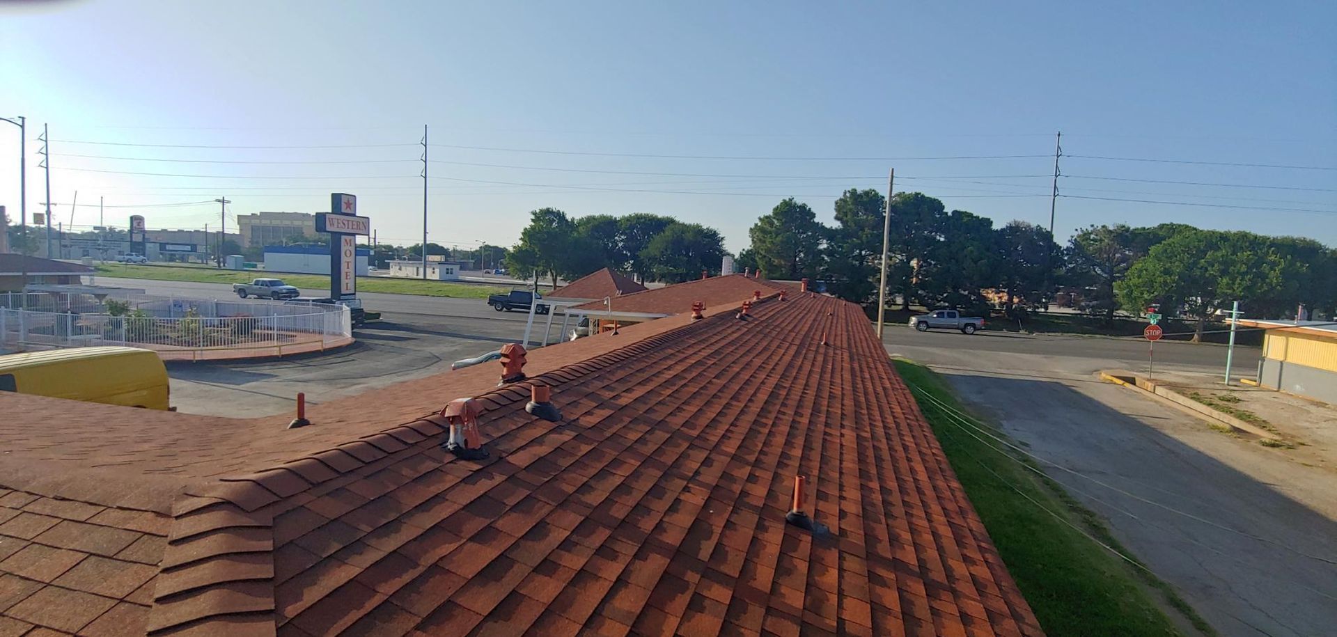 Rooftop with red tiles overlooking a quiet street and buildings under a clear blue sky.