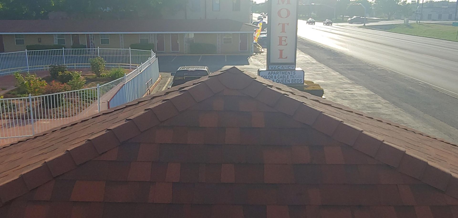 Rooftop view of a road at sunrise, with a brick chimney and hillside fence in the foreground.