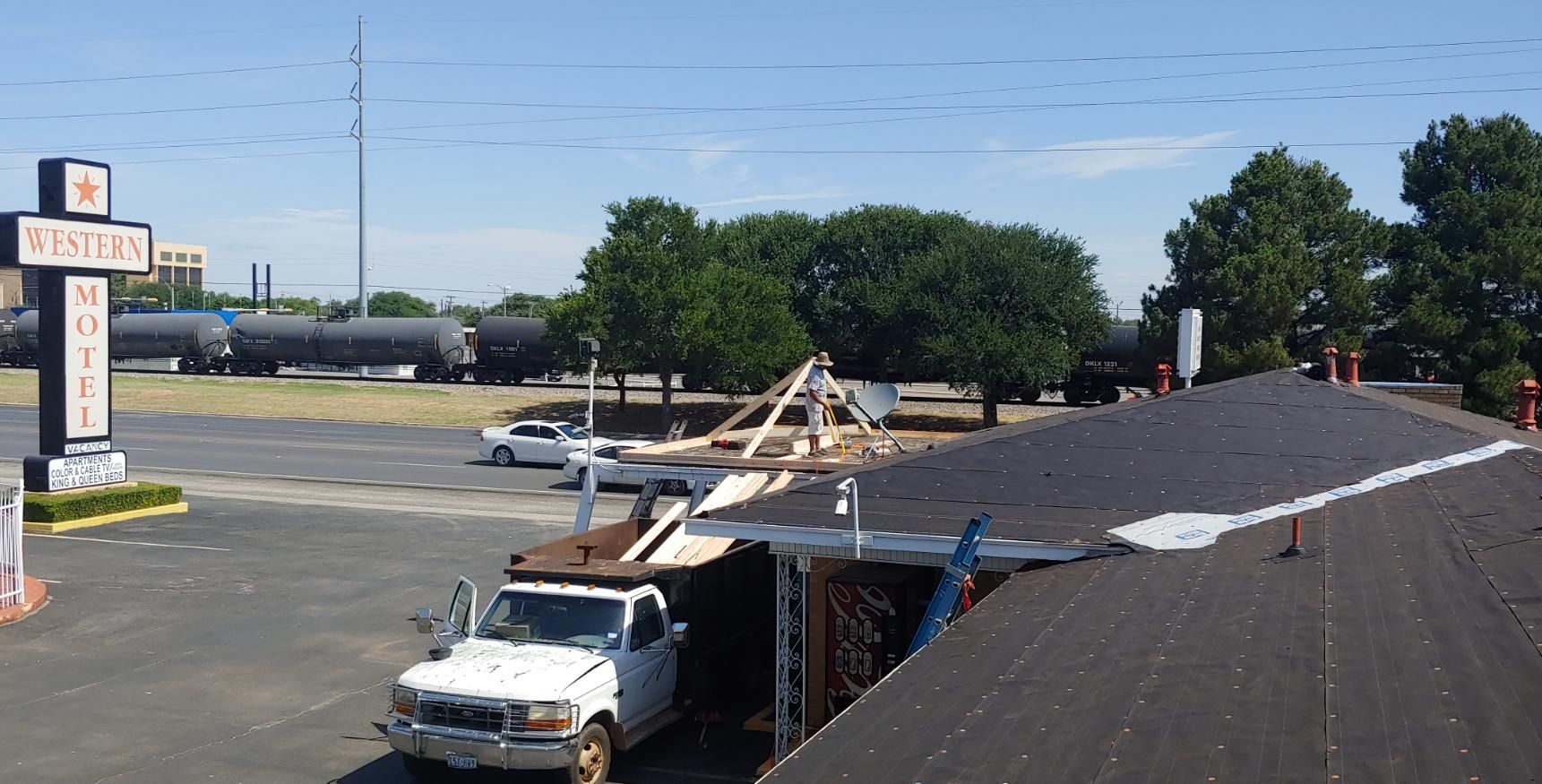 Damaged roof with exposed rafters and a white truck in front of a building near a parking lot
