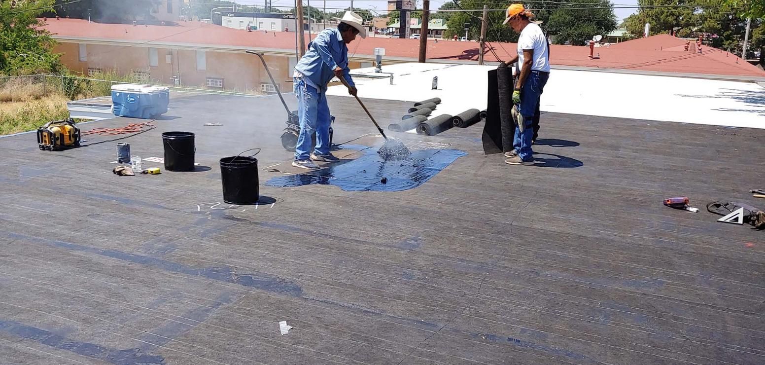 Workers applying blue roofing coating on a flat rooftop with buckets and tools nearby