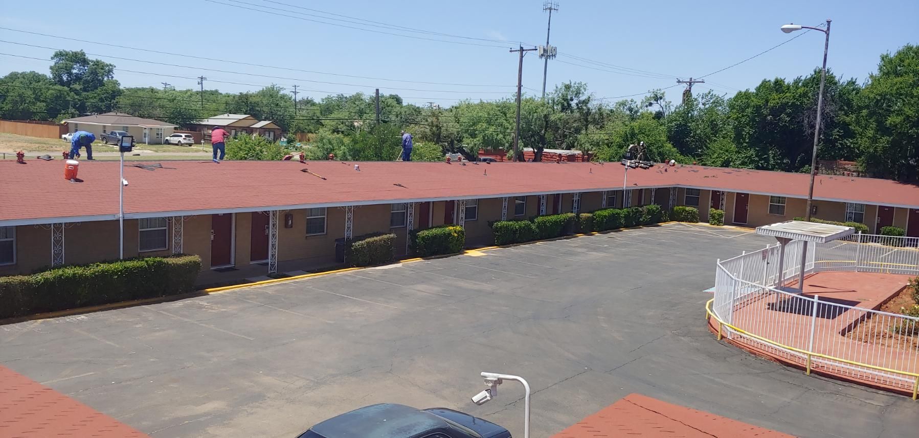 Wide view of a low red-roofed building beside a paved courtyard and trees under a bright sky