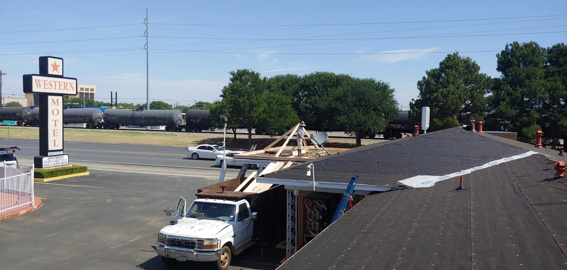 Storm-damaged building roof with a white truck and debris in a parking lot on a sunny day