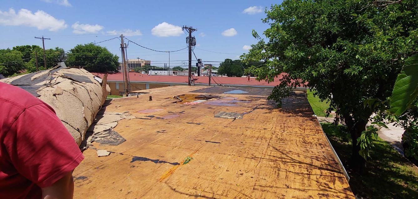 Sunlit damaged rooftop with rusted surface, trees at right, and a person in a red shirt at left edge