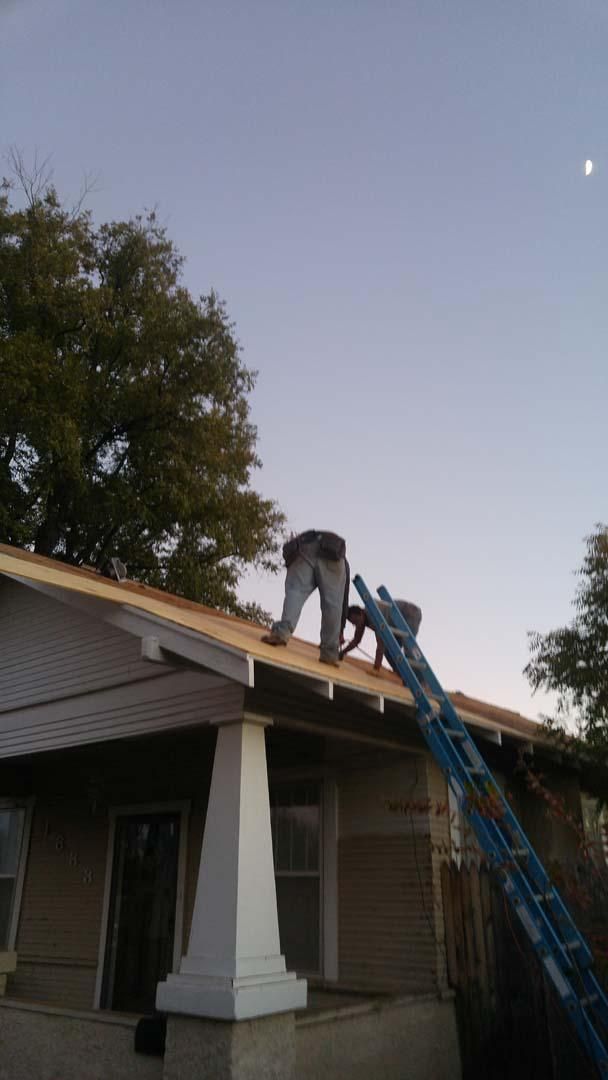 Worker on a blue ladder repairing a house roof at dusk