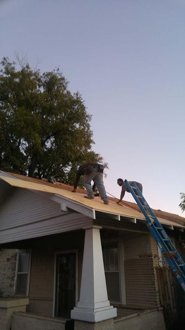 Two workers repairing a roof on a house, with a blue ladder leaning against the edge.