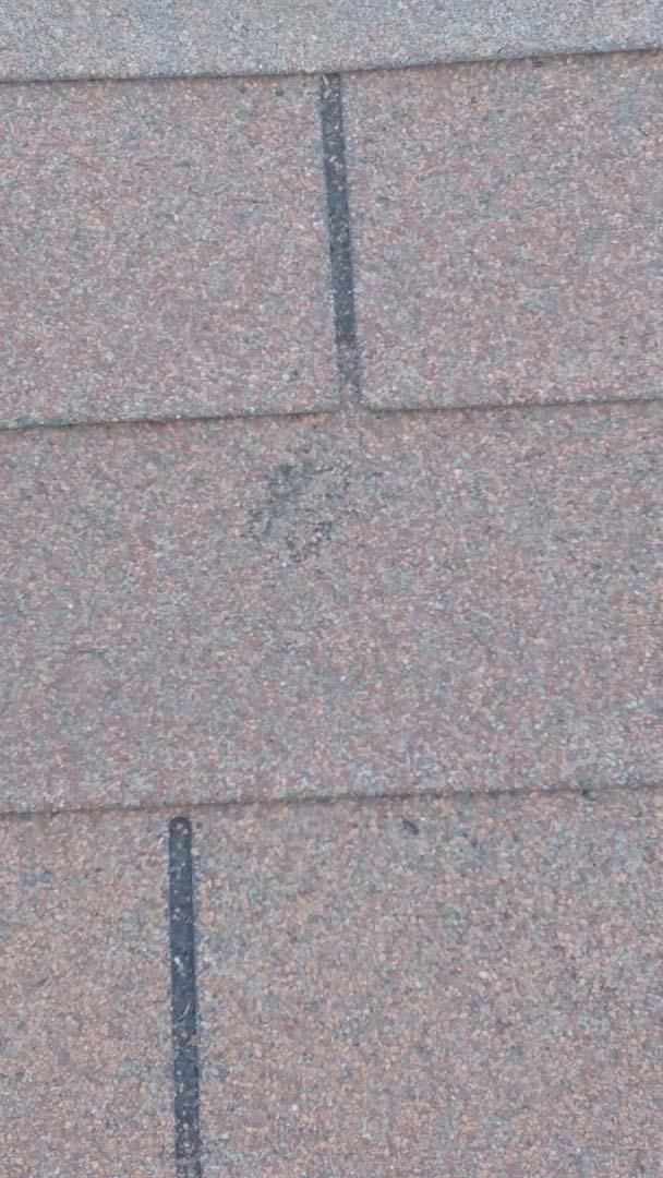 Close-up of pink-brown roof shingles with a dark vertical seam and a small stain.