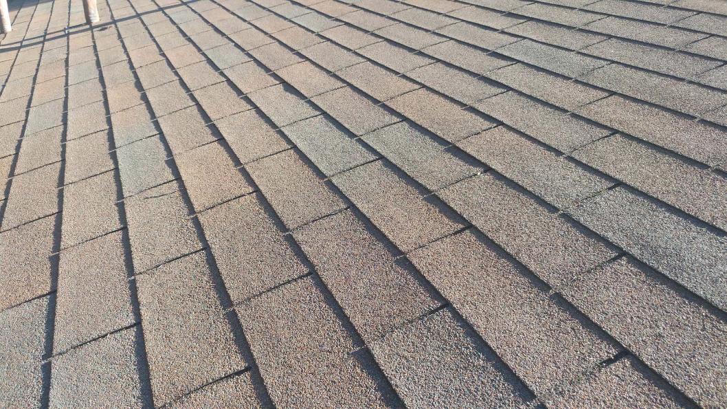 Close-up of a weathered shingled roof with gray-brown textured tiles in sunlight