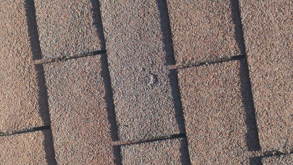 Close-up of a sunlit rooftop with overlapping gray shingles and dark seams