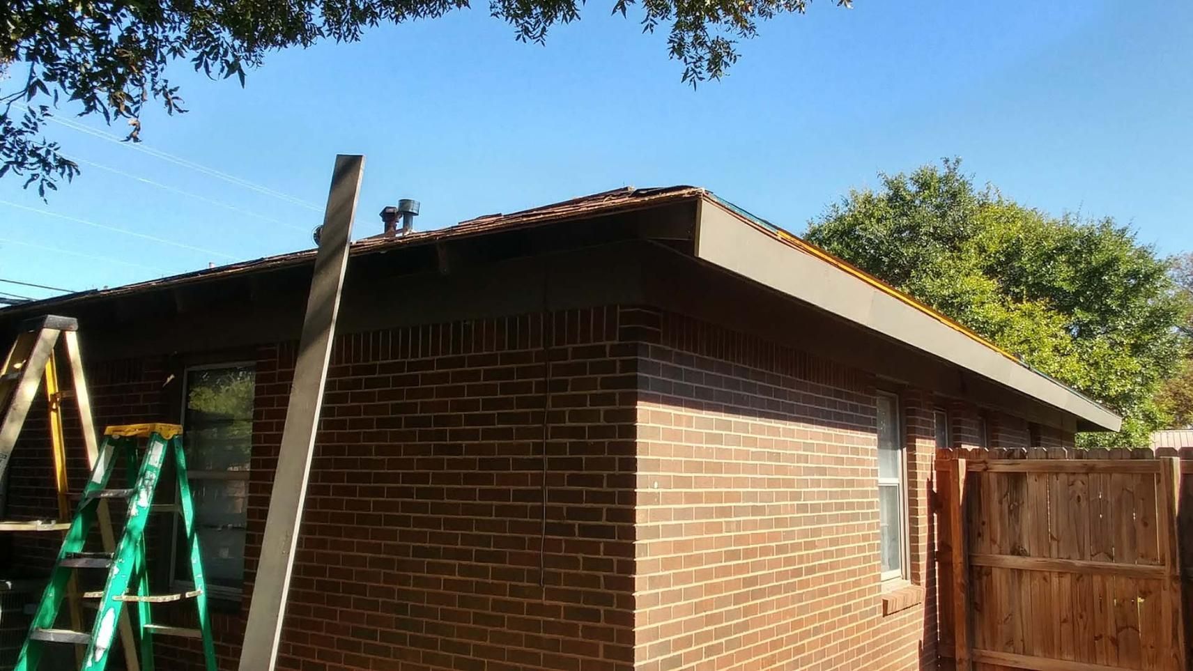 Brick house under construction with a green ladder and wooden fence in the yard