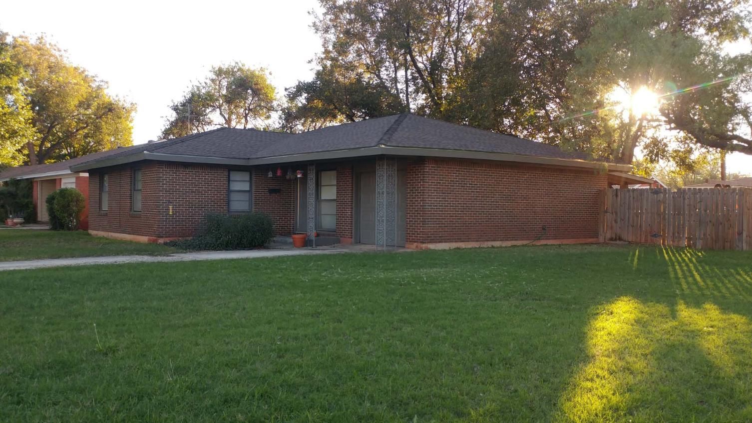 Single-story brick house with a large green lawn at sunset