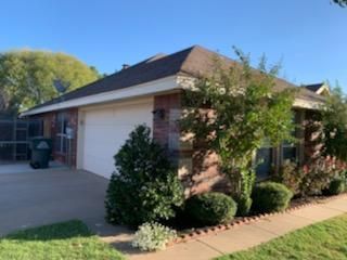 Single-story brick house with garage, driveway, and landscaped front yard under a clear blue sky