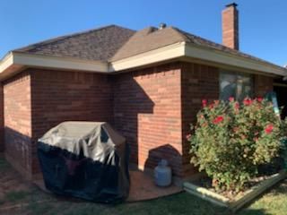 Brick house corner with covered grill, flowering bush, and blue sky