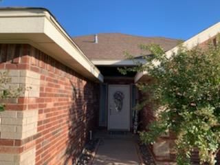 Brick house entryway with a white front door and a bush along the walkway