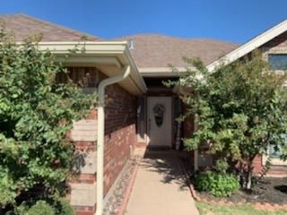 Brick house front entry with a white door, brick walkway, and shrubs under a clear blue sky