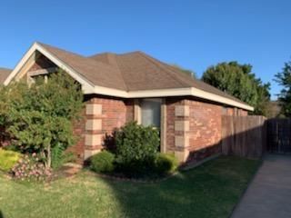 Brick suburban house with a brown roof, front shrubs, and a driveway beside a fenced yard